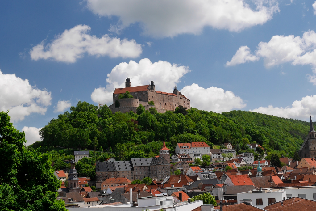 Landschaft mit Hügel und Burg darauf sowie Dort im Tal davor