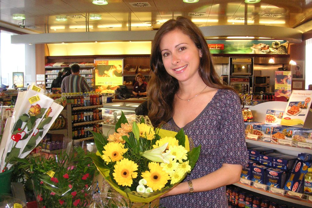 Frau mit Blumenstrauß in Tankstellenshop